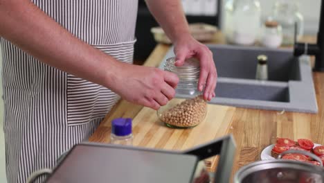 close-up of hands opening a jar of chickpeas in a kitchen