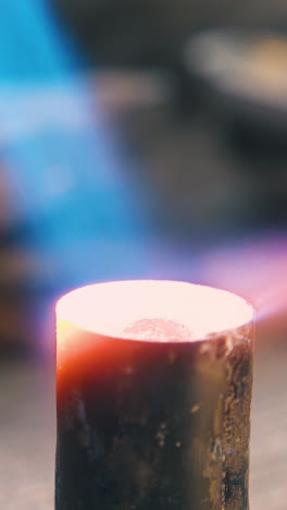 cu: heating of cylindrical metal bar with hot gas burner flame to make detail at workplace in dark workshop extreme closeup