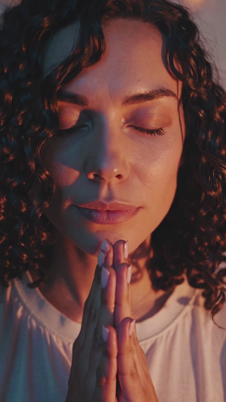 Close-up video still of a serene woman with closed eyes and hands in prayer