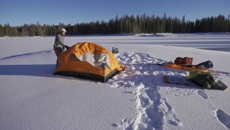 man setting up an orange tent in the snow while camping