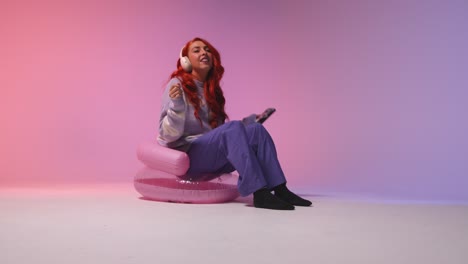 studio shot of young gen z woman wearing headphones streaming music to mobile phone 1