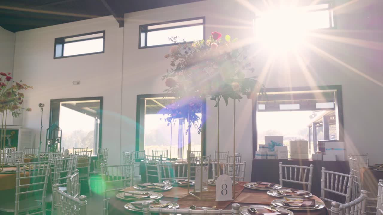 Smooth pull-out from a floral centerpiece close-up to reveal an elegant reception table, bathed in warm sunlight and showcasing beautiful sunflare details.