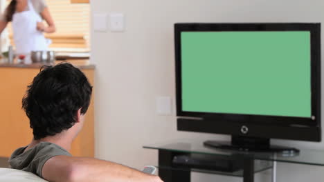 man watching the television while his wife is cooking