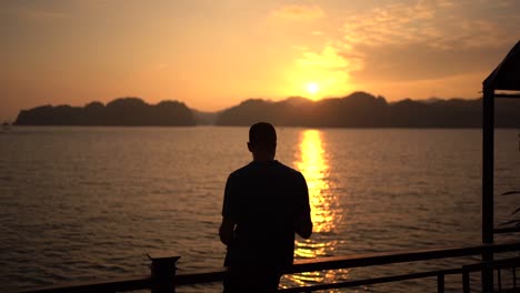 slow motion shot, male silhouette enjoying scenic sunset standing on pier, sunlight reflections on water