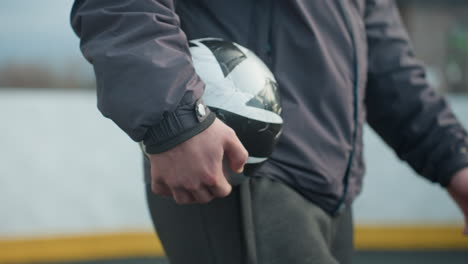 close-up side view of someone walking in sports environment holding black and white soccer ball, showing athletic wear and part of body, with urban background