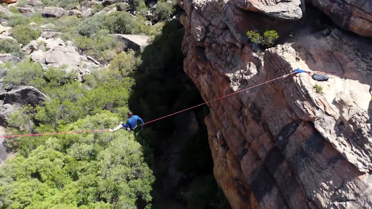 hombre highliner sentado en una cuerda sobre montañas rocosas 4k