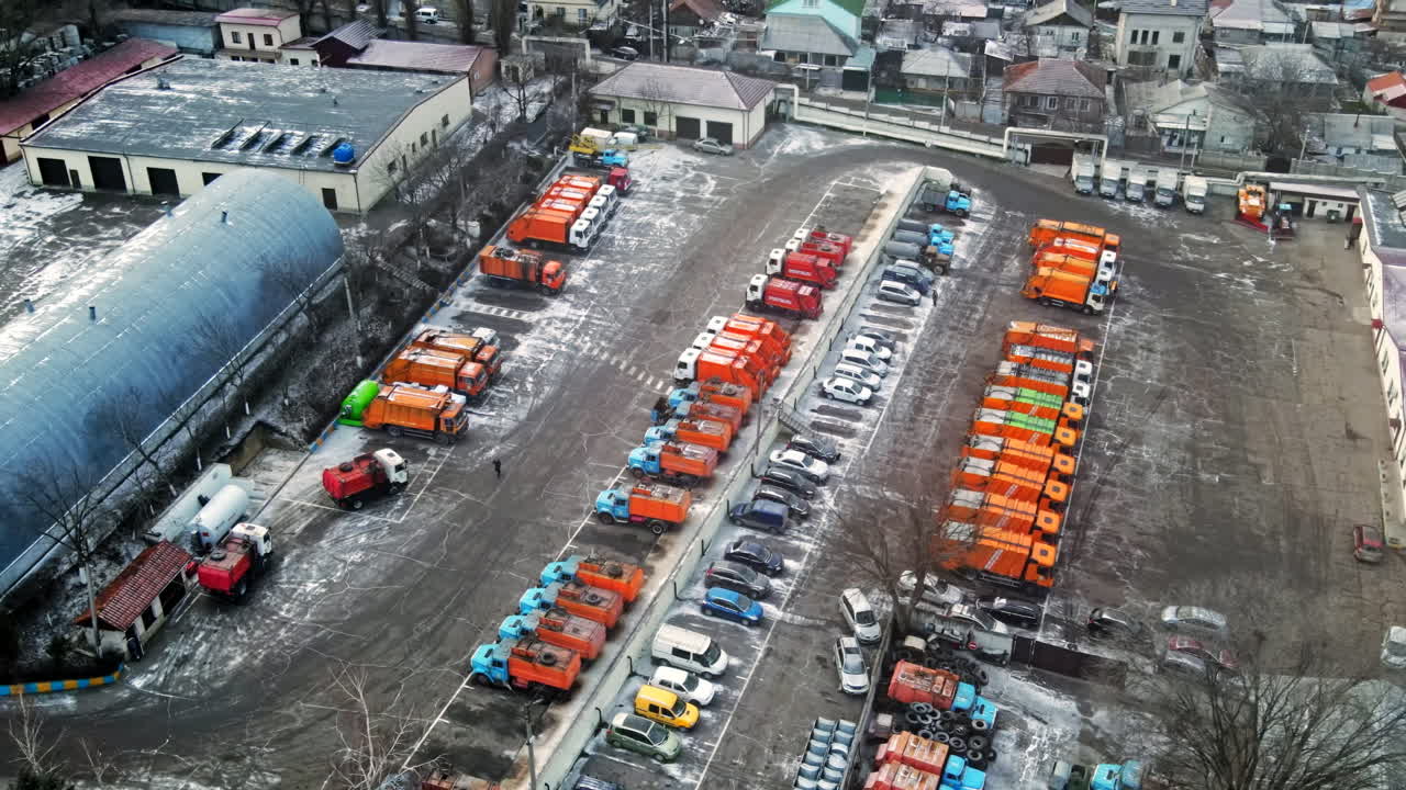 Aerial drone view of industrial zone in Chisinau, Moldova. Multiple parked garbage trucks, hangars, Cloudy weather, bare trees, winter