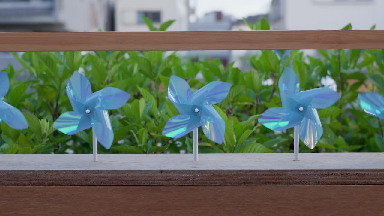 A close-up shot capturing vibrant blue pinwheels rapidly spinning in a gentle breeze, adorning the promenade railing at Tokyo Mizumachi along the Kita-jūkken-gawa River