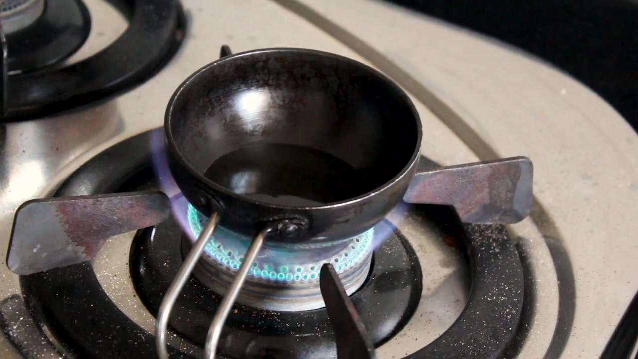 Piccola padella tadka in ferro riscalda l'olio su fiamma a gas blu per il soffritto indiano tradizionale. Perfetto per documentari culinari, video di ricette e contenuti di cucina sud-asiatica