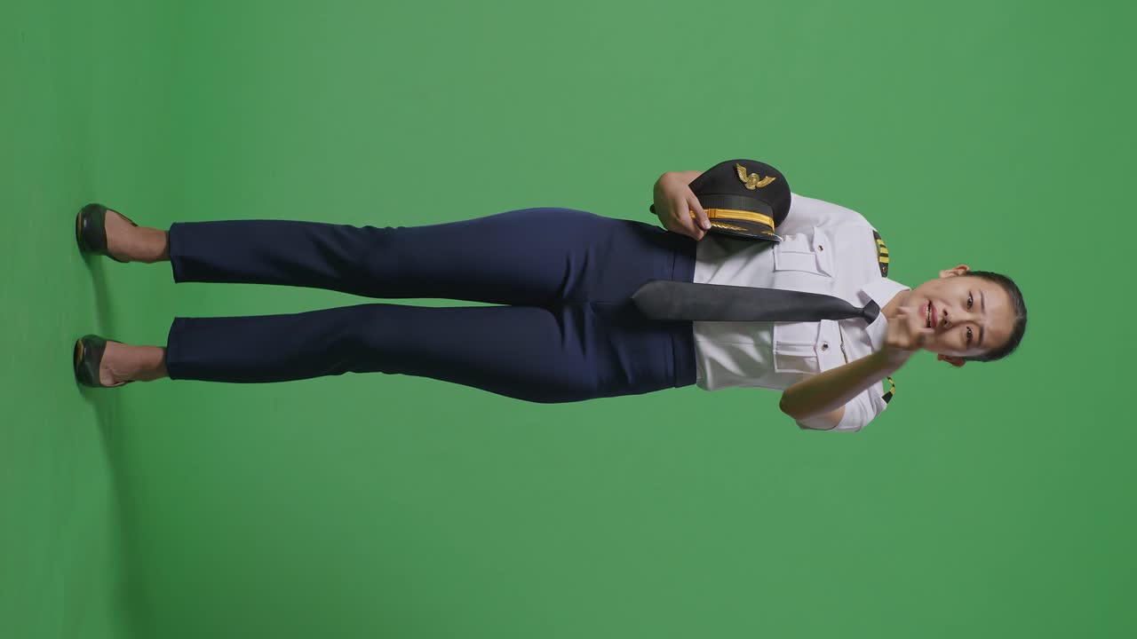 녹색 스크린 배경 스튜디오에 서 있는 동안 카메라에 소리치는 아시아 여성 조종사의 몸이 가득 차 있습니다.