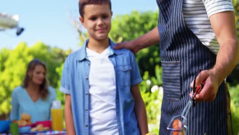 padre e hijo asando salchichas y maíz en la barbacoa