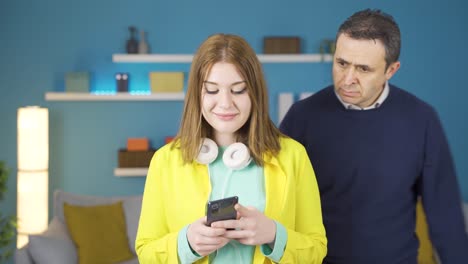 девочка с наушниками смеется и пользуется телефоном. его отец злится на него.
