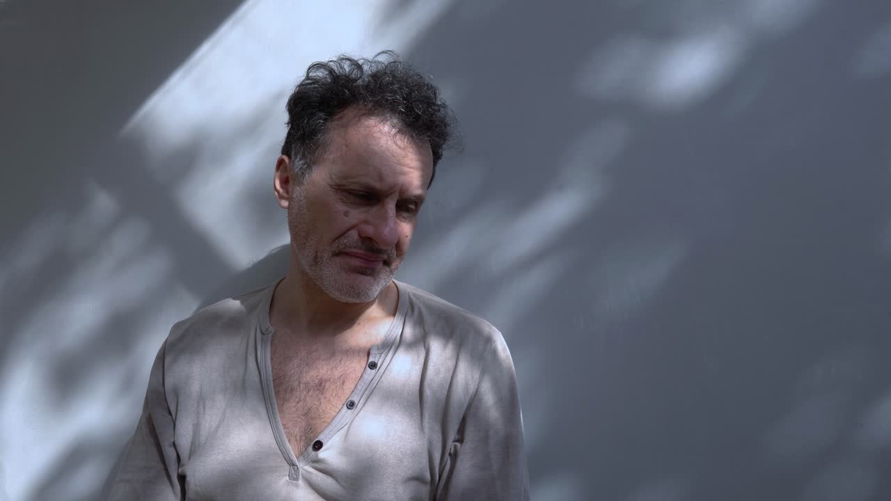 un hombre en una pared con una expresión preocupada, sus manos presionadas contra su cara, perdido en sus pensamientos