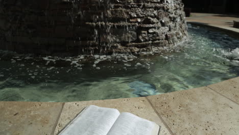 Heiliges-Buch-Vor-Einem-Friedlichen-Wasserfontänen-Hintergrund:-Schwenk-Nach-Oben