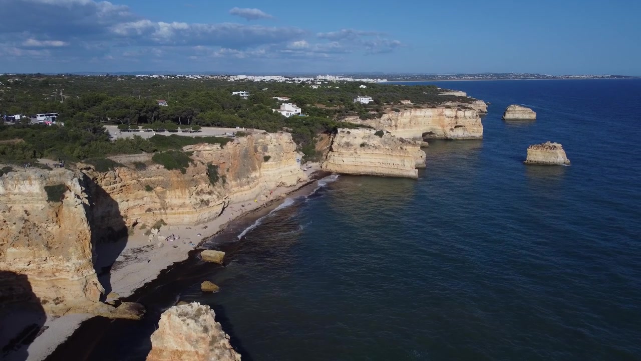 Een luchtfoto toont de Algarve-regio van Portugal. Ruige gouden kliffen ontmoeten de helderblauwe Atlantische Oceaan onder een stralende, zonnige hemel.
