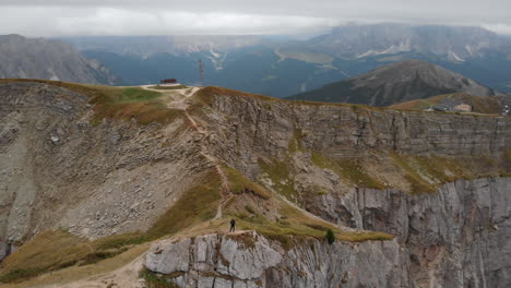 Aerial-circular-shot-from-a-drone-of-an-young-male-model-standing-on-the-edge-of-a-rock-in-Seceda,-Italy