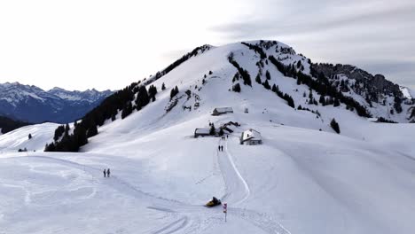 Cinematic-drone-shot-showing-walking-people-and-snowmobile-on-snowy-path-in-swiss-mountains---Aerial-orbiting-shot