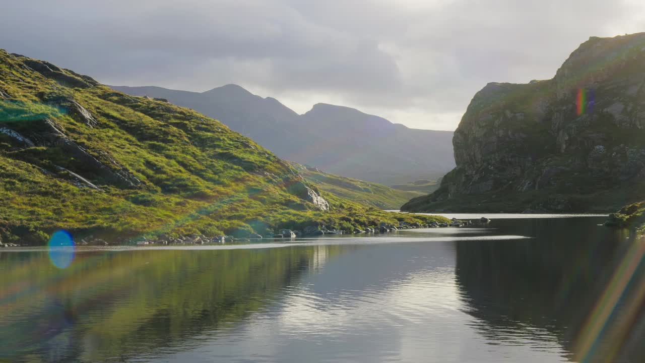 Highland gorge and loch on a calm morning, with dramatic lens flares over moorland and mountains