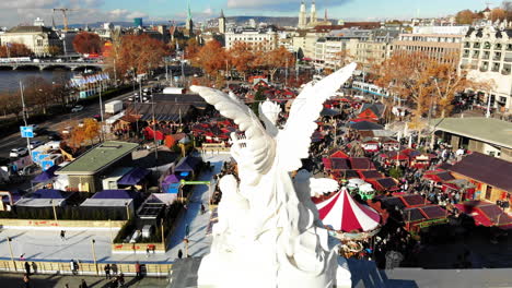 Drone-shot-revealing-the-Christmas-Market-in-Zurich,-Switzerland-behind-an-Angel-statue-of-the-Opera-House