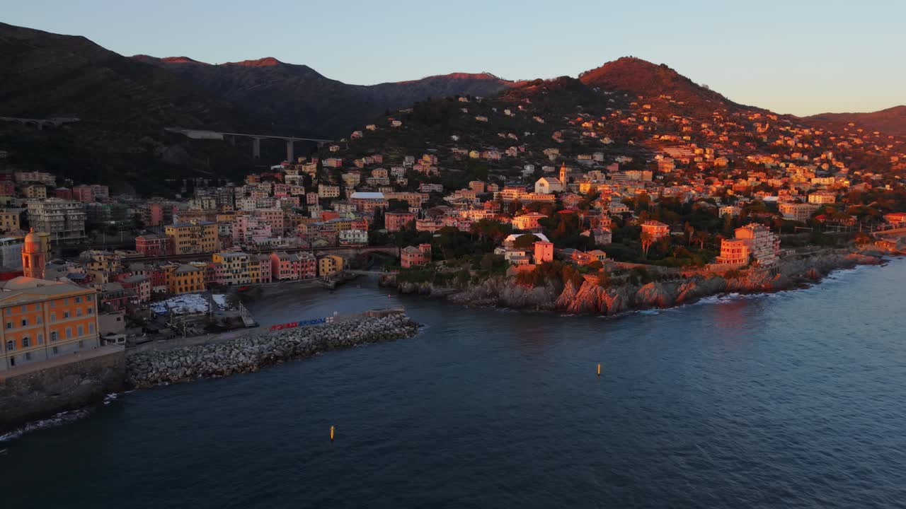 Golden hour view of Genoa's coastline, with city buildings and rocky shores