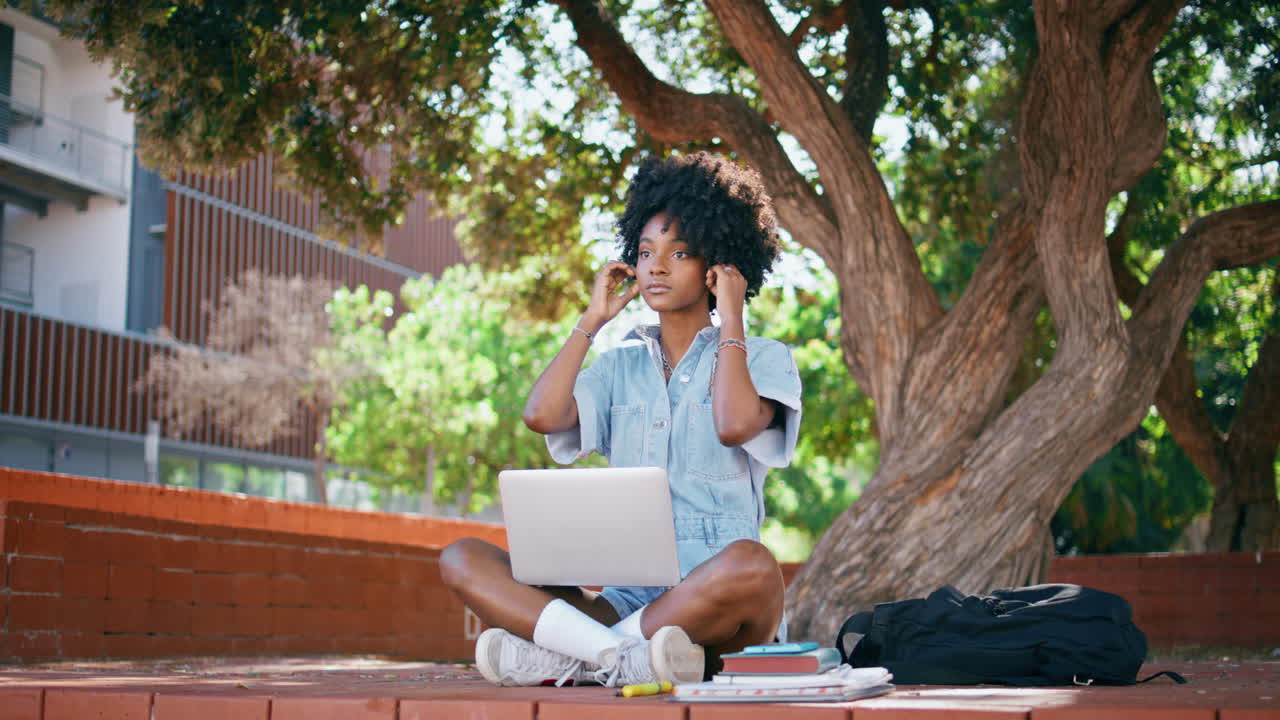 chica adolescente con auriculares sentada bajo un árbol con una computadora portátil. estudiante