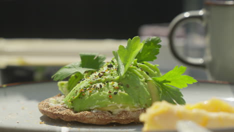 Morning-Delight:-Slow-Motion-Close-Up-of-Avocado-on-Crispbread-at-Sunlit-Breakfast-Table