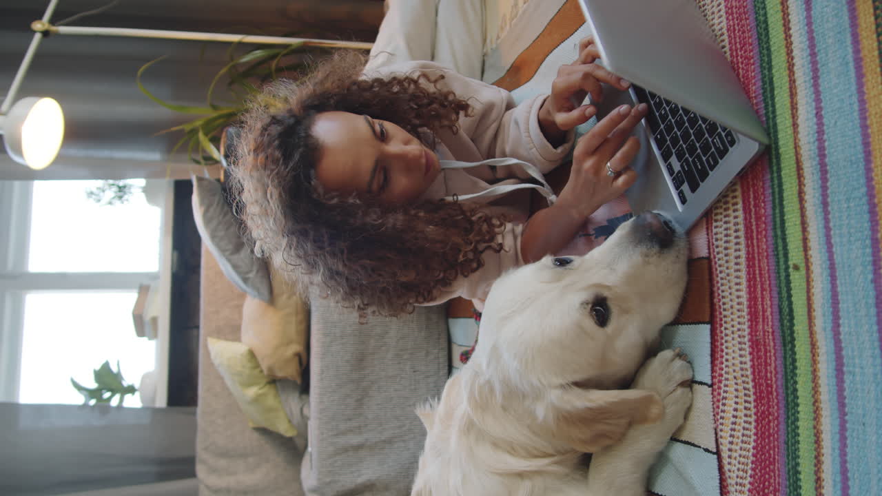 mujer trabajando en una computadora portátil mientras se relaja con un perro en una cama