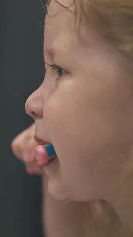 funny little girl with blonde hair brushes teeth without paste in light bathroom at home close side view