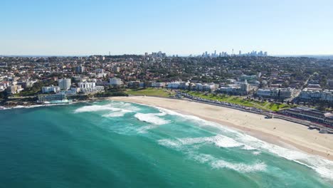 Luftaufnahme-Von-Wellen,-Die-Im-Sommer-Am-Sandufer-Von-Bondi-Beach-Mit-Stadtbild-Kommen---Bondi,-Nsw,-Australien