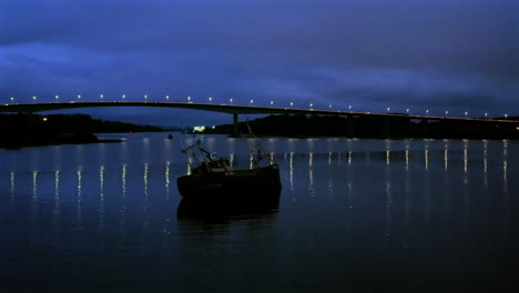 aerial orbit of foyle bridge at night with traffic and a small fishing boat in the foreground.