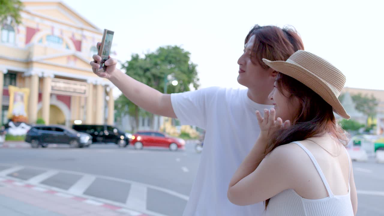 Una giovane coppia asiatica sorridente scatta un selfie con uno smartphone in una strada di Bangkok