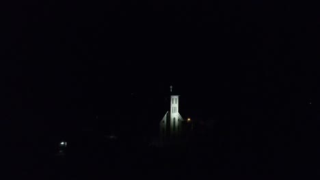 a reveal of a catholic church with a bell tower lit up at night placed on top of a hill in a small community in wisconsin