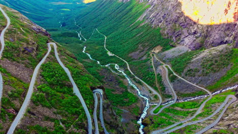 tilting aerial shot of a car driving along the trollstigen with waterfalls