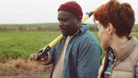 diverse farmers walking with tools through field and speaking