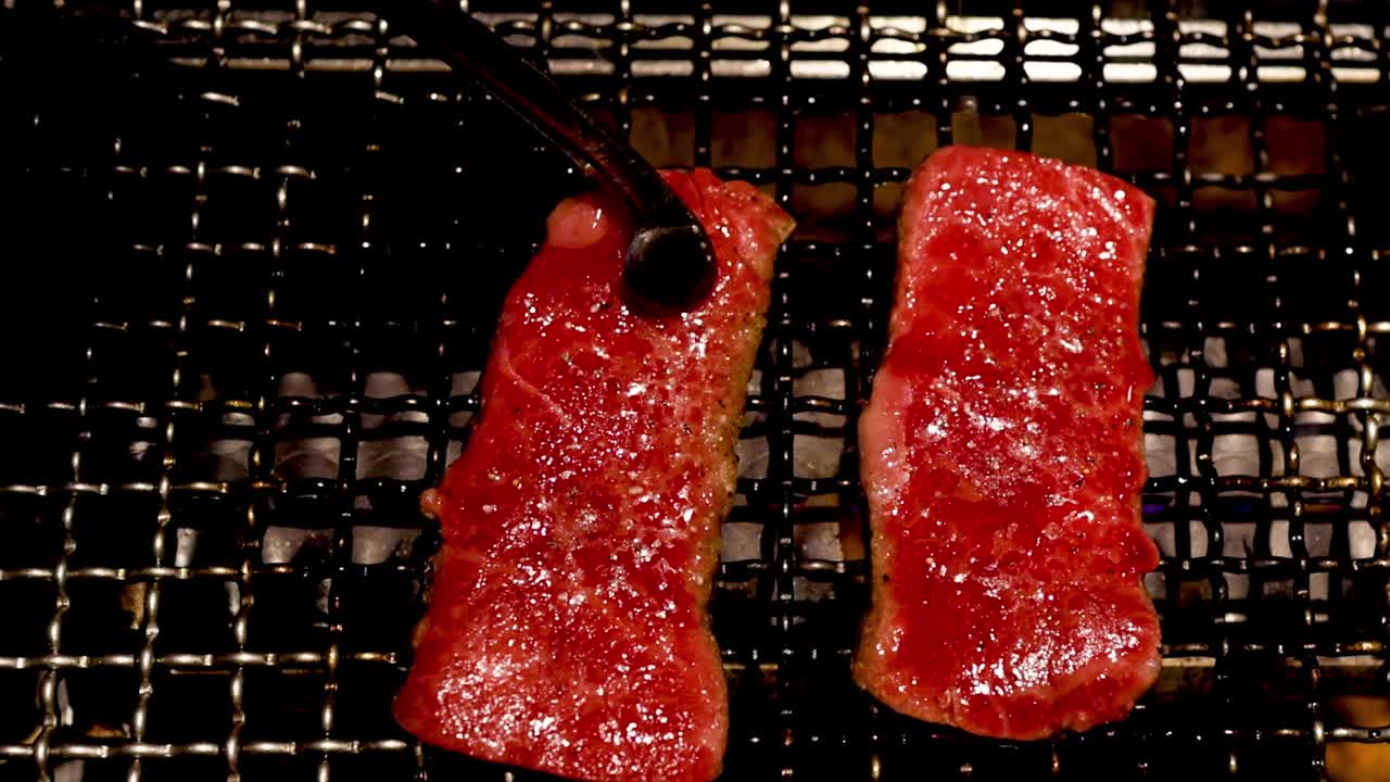 A detailed view of steaks being flipped on a grill, highlighting the cooking process and texture change.