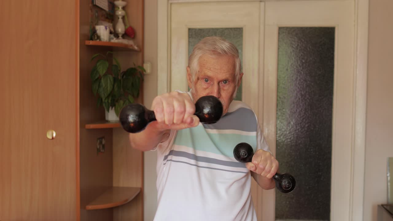 고령 백인 남자가 집에서 덤벨로 운동을 하고 있습니다.
