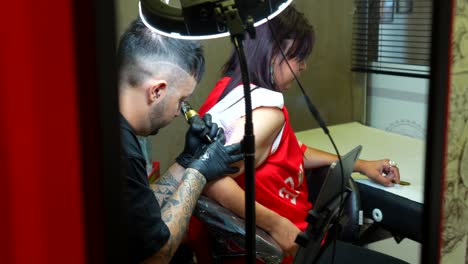 mirror reflect of a woman being tattooed by an artist in a professional studio