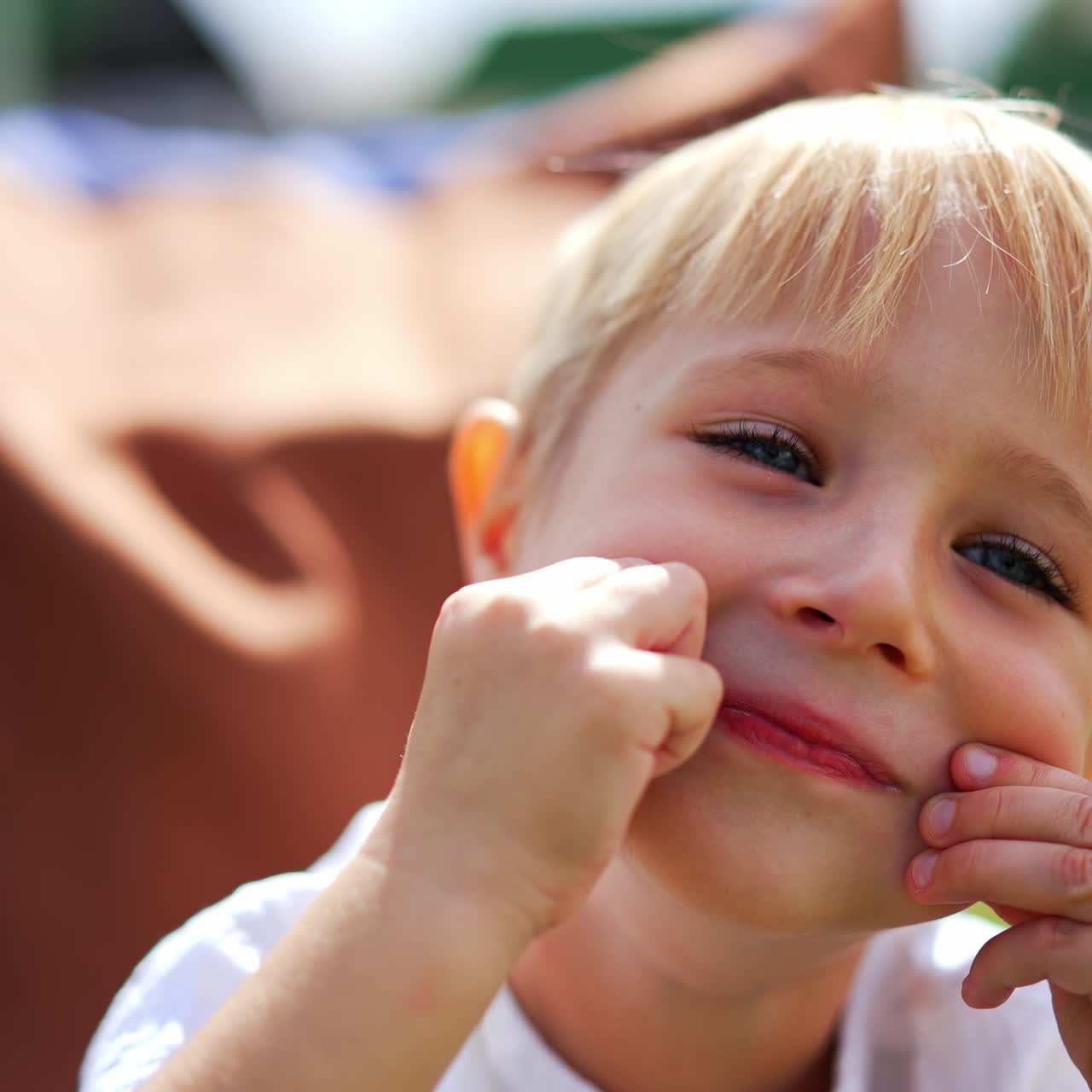 Five-year-old boy making faces sitting outdoors. Little kid having fun resting in bean bag chair in the bright sun. Close up
