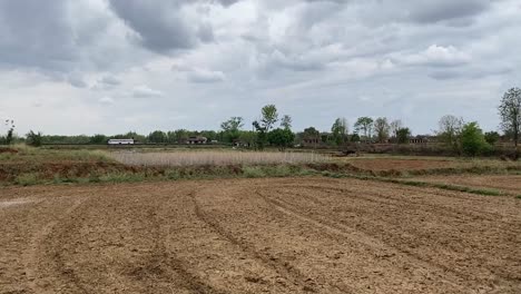 wide shot of a recently ploughed farm in a village in jharkhand, india in a cloudy weather