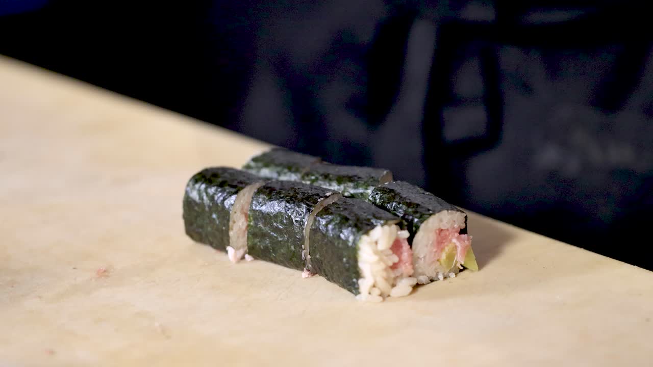 Close-up shot of a chef's hands meticulously plating sliced maki sushi rolls on a board