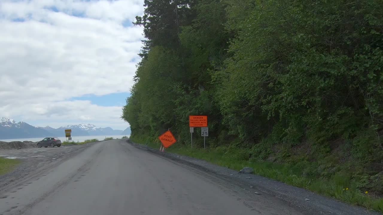 POV - Driving on Lowell Point Road that is a gravel road that runs along a tree-covered mountain side and drops off to the ocean bay; near Seward, Alaska