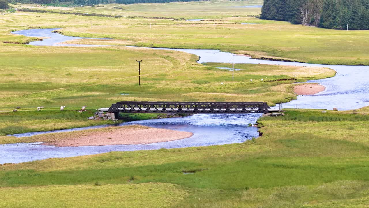 Passenger train travels across rural bridge, lush green valley, winding river, daylight, wide shot