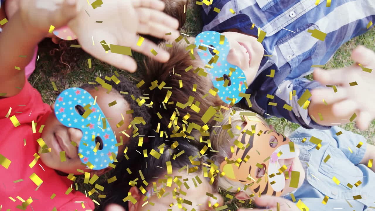con máscaras, niños acostados en la hierba con animación de confeti cayendo a su alrededor