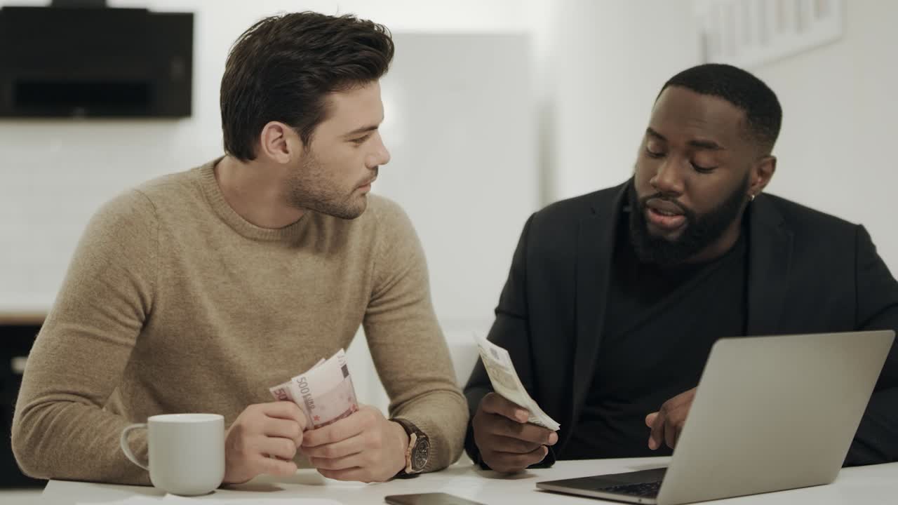 Two business men sitting at open kitchen with money in hands.