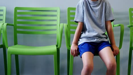 upset boy sitting on chair in hospital corridor