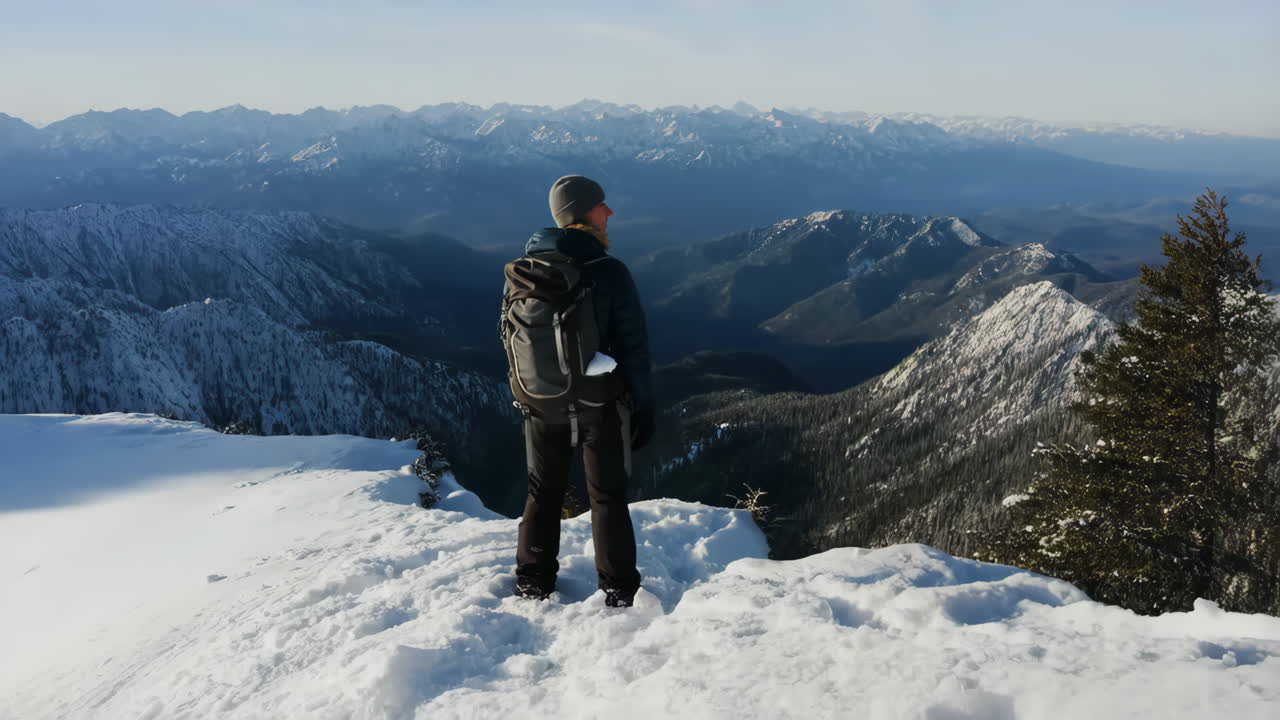 Hiker on snowy mountain peak overlooking vast winter landscape