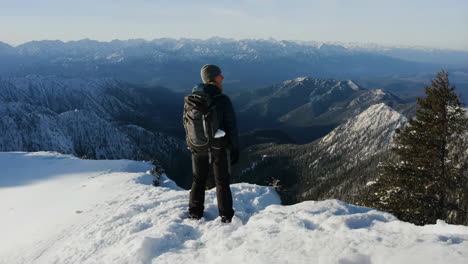 hiker on snowy mountain peak overlooking vast winter landscape