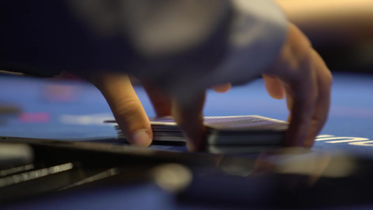 Close-up shot of a poker dealer shuffling playing cards at a casino table. Gambling, poker, card game and casino entertainment concept footage