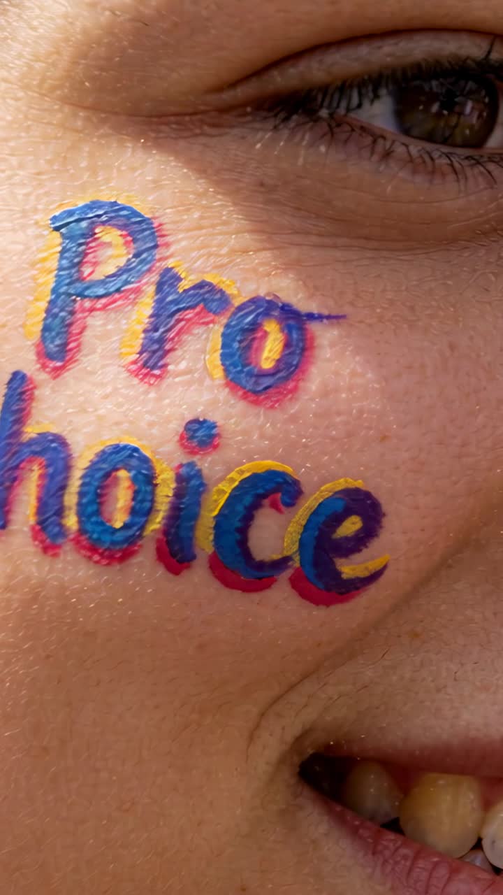 Vertical video: Camera zooming in, woman smiling, revealing Pro choice cheek paint detail outdoors