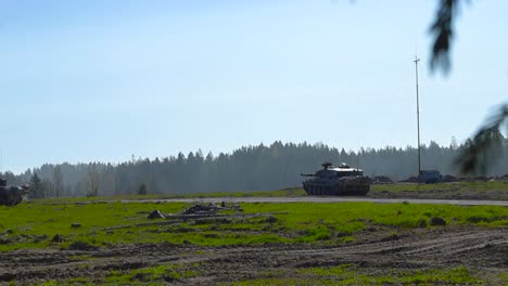 rare video of multiple british challenger 2 4034 tanks aiming at enemy troops on a green grasy field while sun is shining during summer. filmed from behind some bokeh blurry forest branches moving.